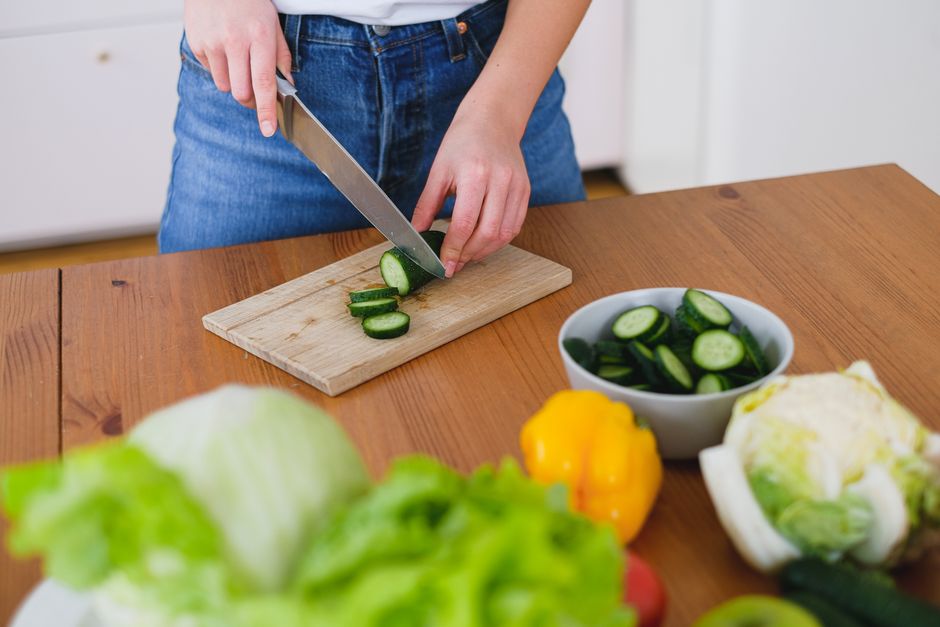 Healthy food preparation with fresh cucumbers and vegetables on a wooden table.