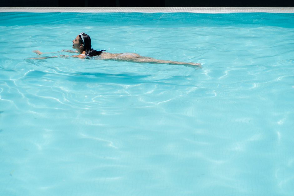 Side view full body of female tourist swimming in pool with crystal clear water at resort