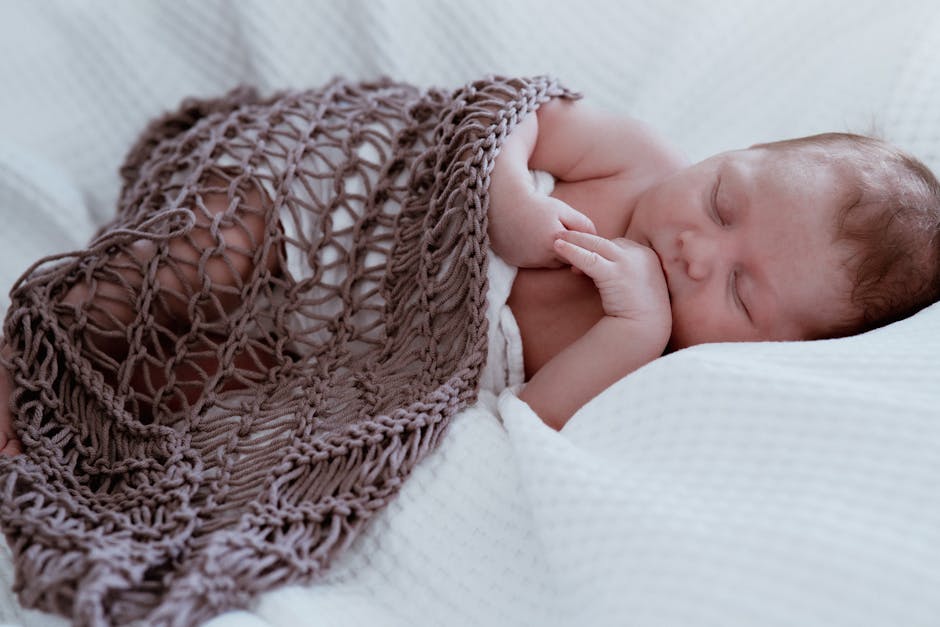 A serene close-up of a newborn baby sleeping peacefully under a knitted blanket.