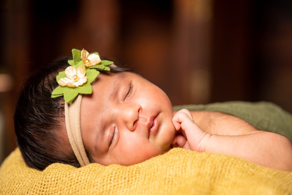 Close-up of a peaceful sleeping newborn baby wearing a floral headband indoors.