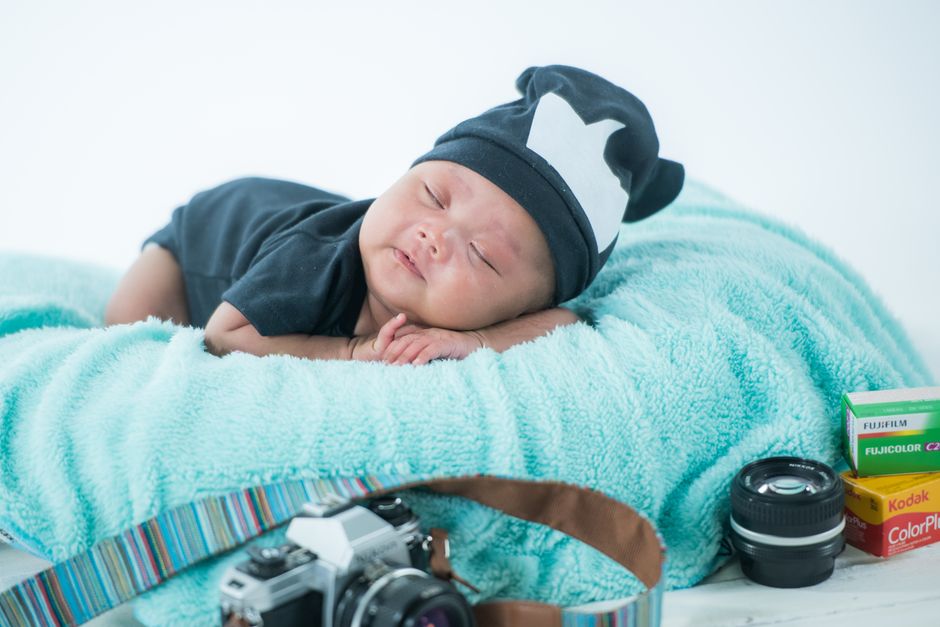 Cute sleeping baby with camera gear on a cozy blanket in a studio setting. Perfect for newborn photography themes.