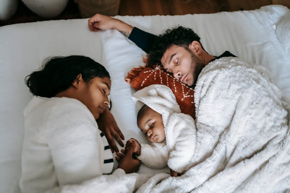 Top view of peaceful multiracial family with adorable newborn baby lying and sleeping on soft cozy bed in daylight