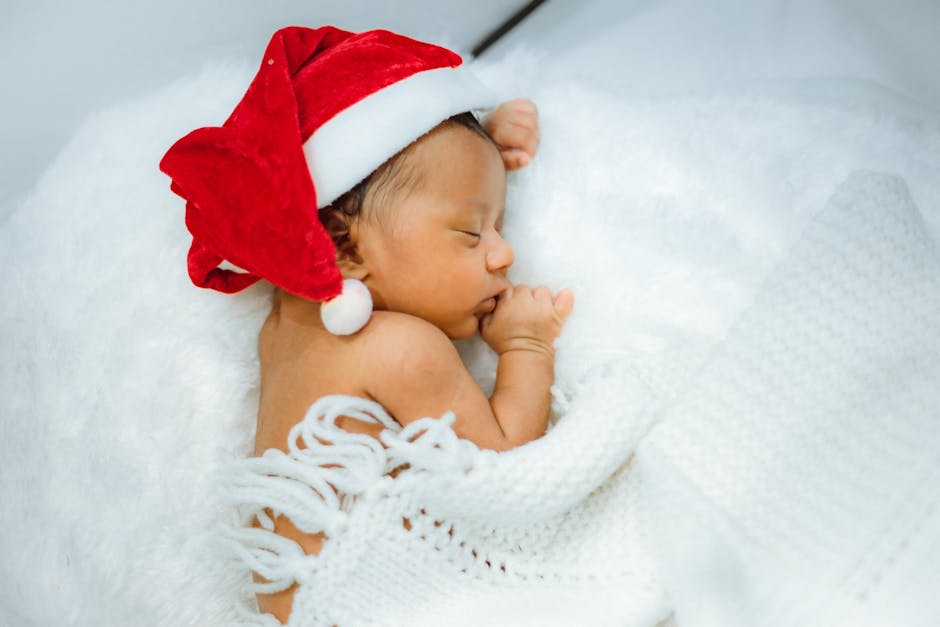 Cute newborn baby wearing a Santa hat and sleeping peacefully in soft white blankets.
