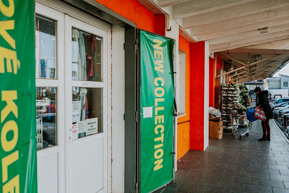Street scene featuring a storefront with new collection signage and a person walking by.