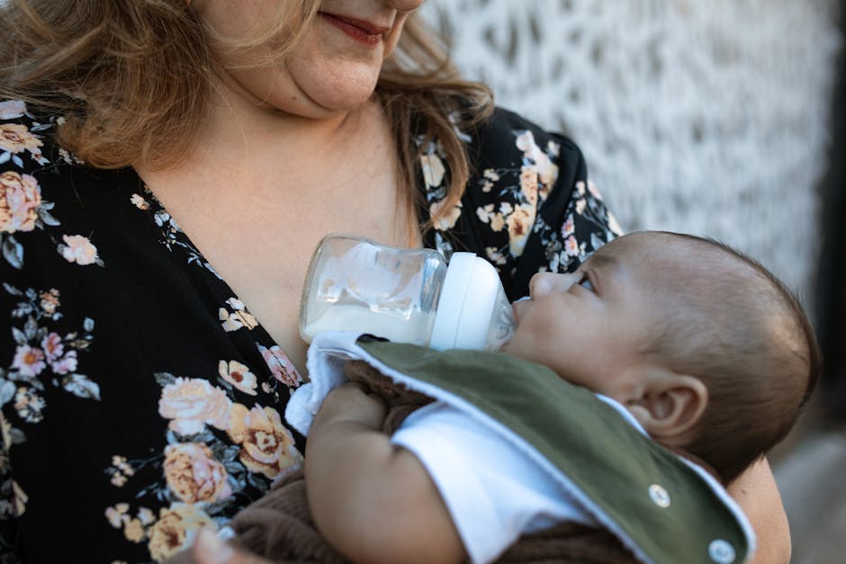 A caring mother feeding her baby with a milk bottle outdoors, capturing the essence of motherhood.