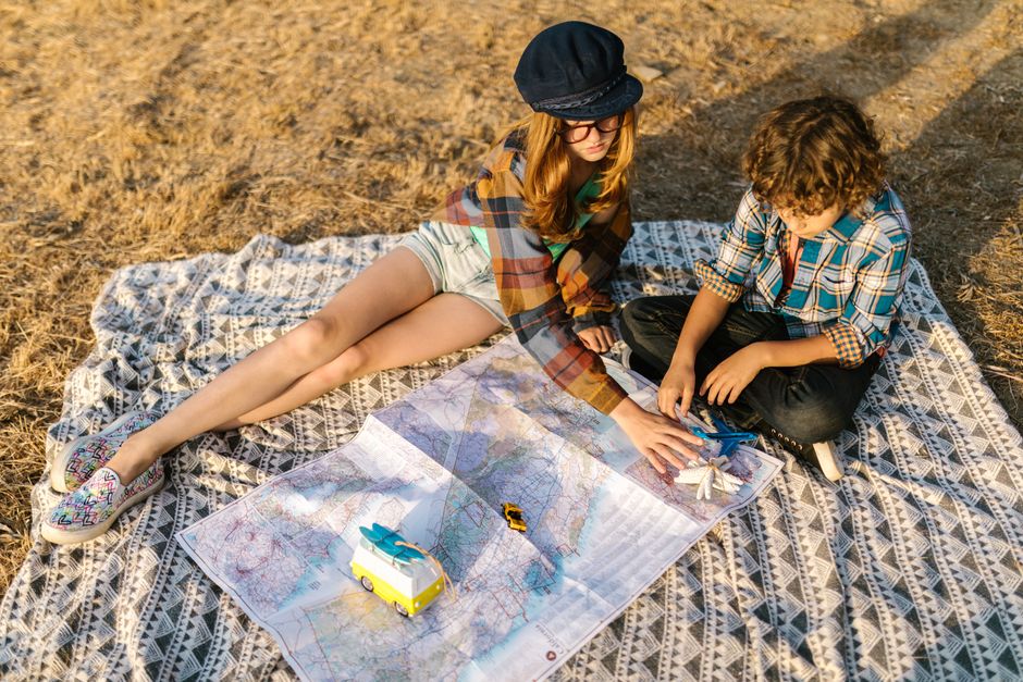 Two kids on a blanket exploring a map outdoors, dreaming of travel adventures.