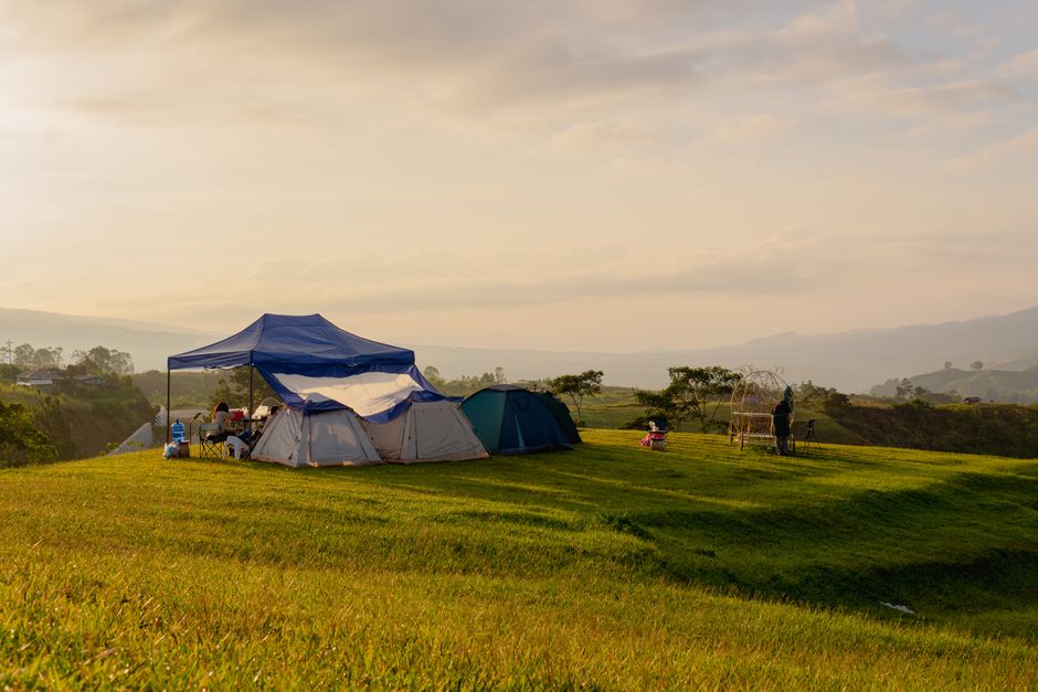 Idyllic outdoor camping scene with tents, people, and a sunset view over rolling hills.