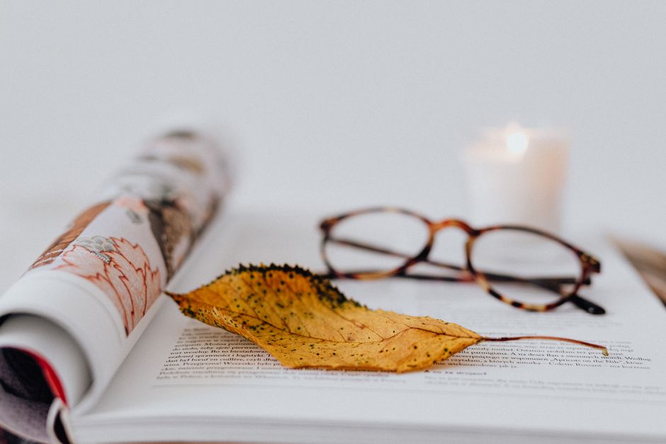 Aesthetic arrangement of eyeglasses on an open book with dried leaf, candlelight ambiance.