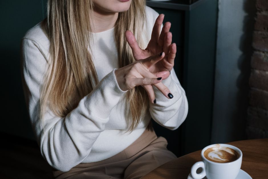 Close-up of a woman gesturing in sign language with a latte in focus, illustrating communication and lifestyle.