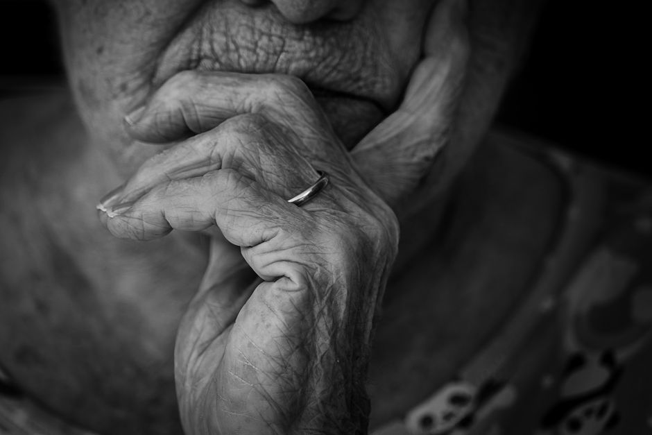 Black and white portrait of a senior adult in deep contemplation, focusing on hands and facial expression.
