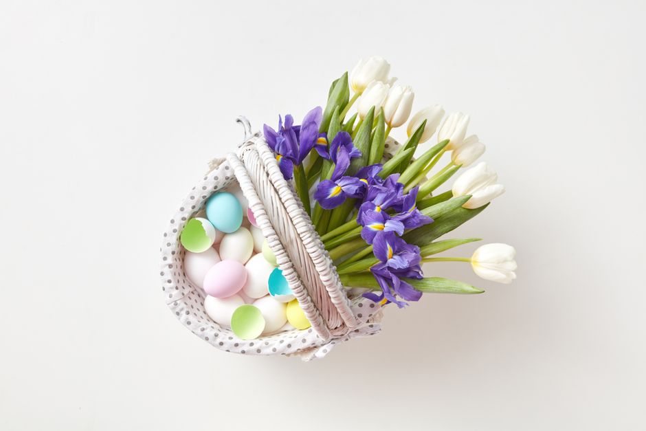 Top view of a wicker basket with colorful Easter eggs and fresh spring tulips and irises.