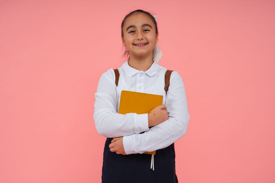 A cheerful schoolgirl holding a book against a bright pink background, symbolizing education.