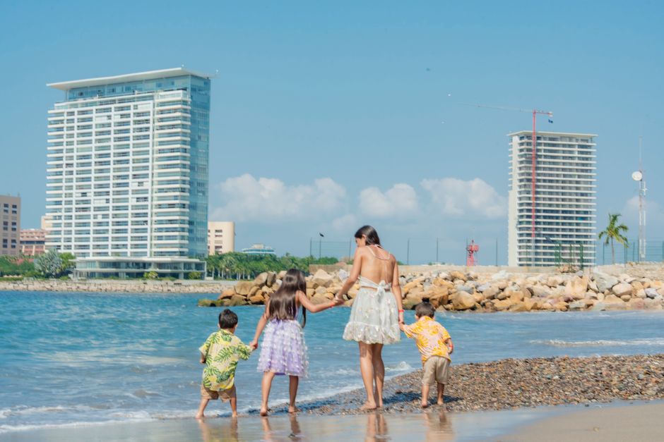 A happy family playing on a sandy beach with modern buildings in the background on a sunny summer day.