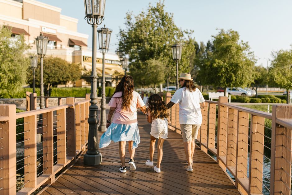 A family walking together on a wooden bridge in a sunny park setting.