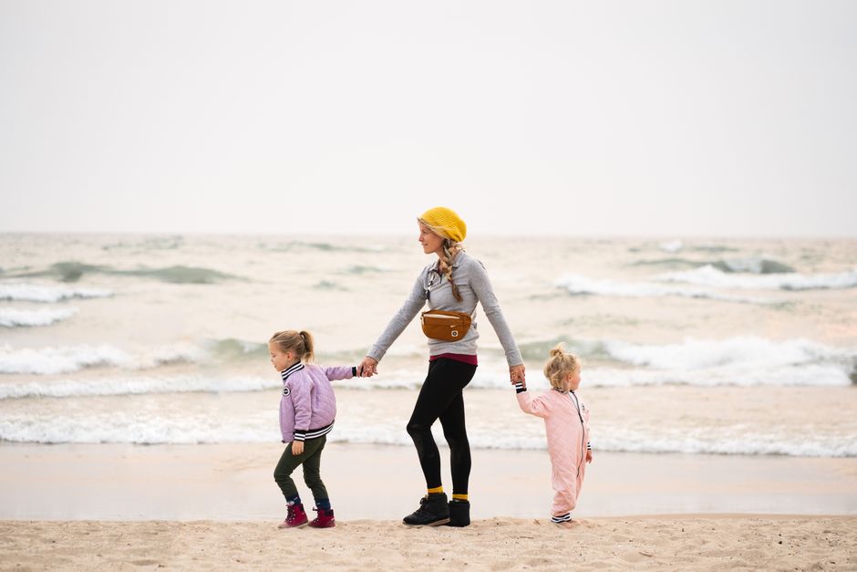 A mother walks hand-in-hand with two young daughters on Grand Haven Beach, Michigan.