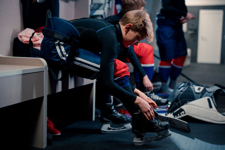 Teenagers in hockey gear preparing in a locker room, lacing up skates and adjusting protective gear.