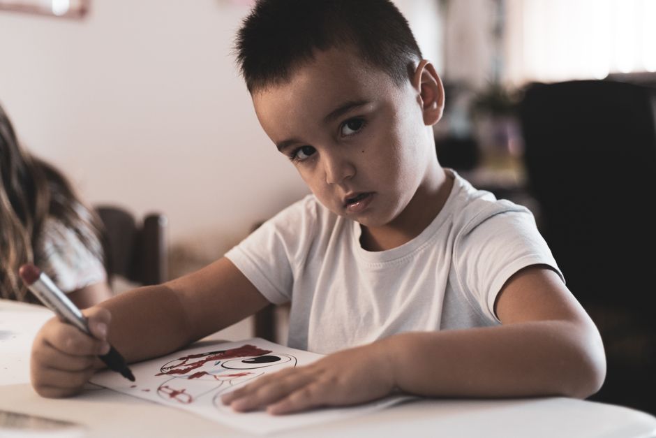 Focused young boy drawing with a marker indoors, showcasing creativity and concentration.