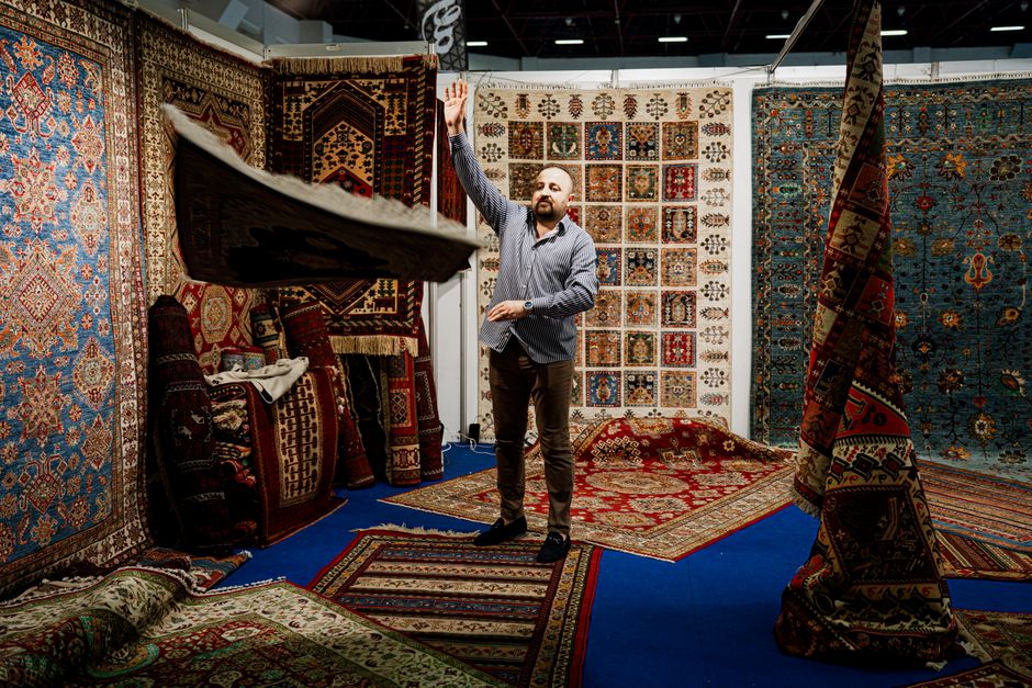 A man showcases traditional Persian rugs at an indoor market stall.