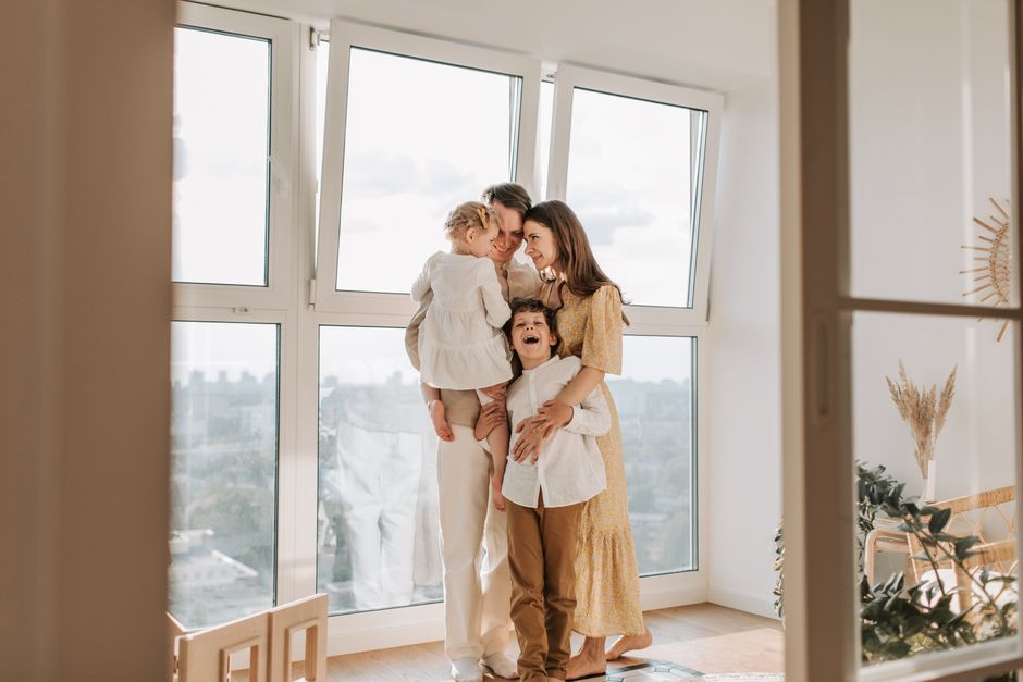 A loving family embraces near a large window in a bright, airy room, exuding warmth and togetherness.