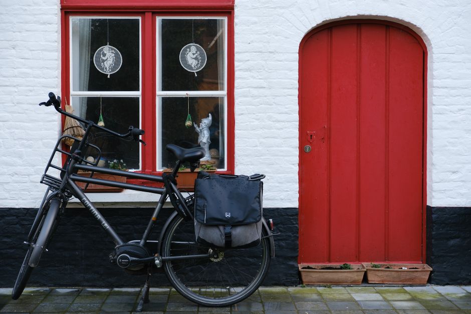Black bicycle parked by red door and windows of a white house