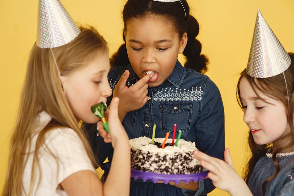 Three girls celebrating a birthday with cake and party hats against a yellow background.