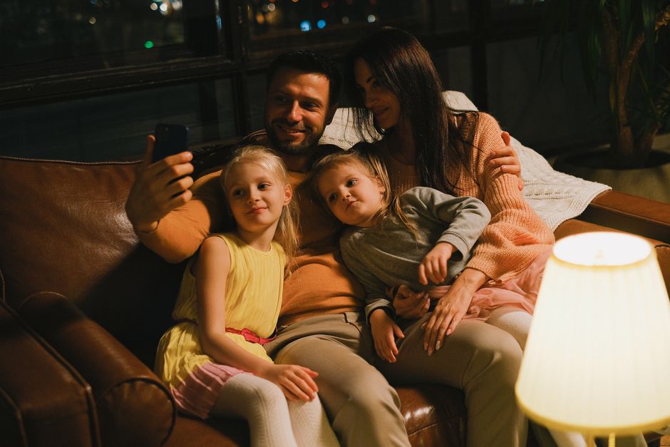 A joyful family of four taking a selfie on a cozy couch during the evening.