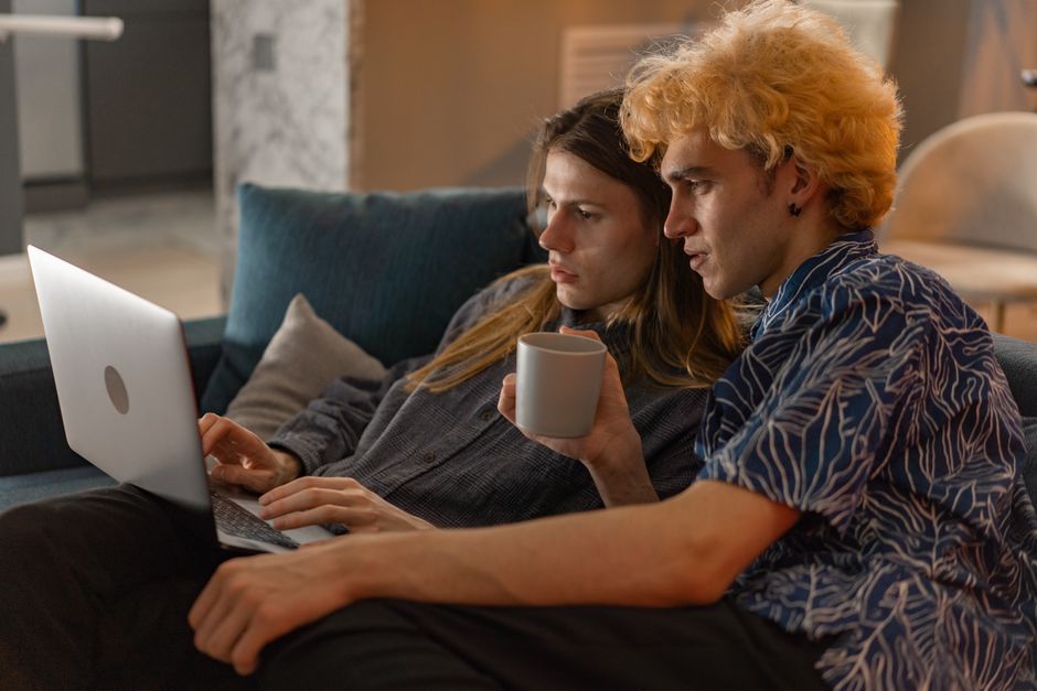 Couple relaxing on a sofa, enjoying a laptop and a warm drink, showcasing love and togetherness.