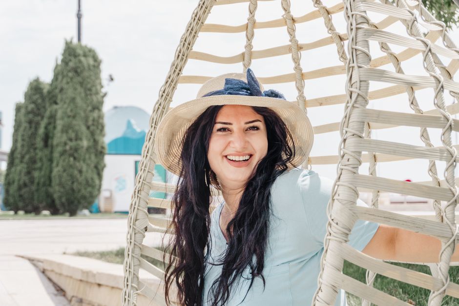 Happy woman sitting on a swing outdoors in Baku, Azerbaijan, wearing a straw hat.