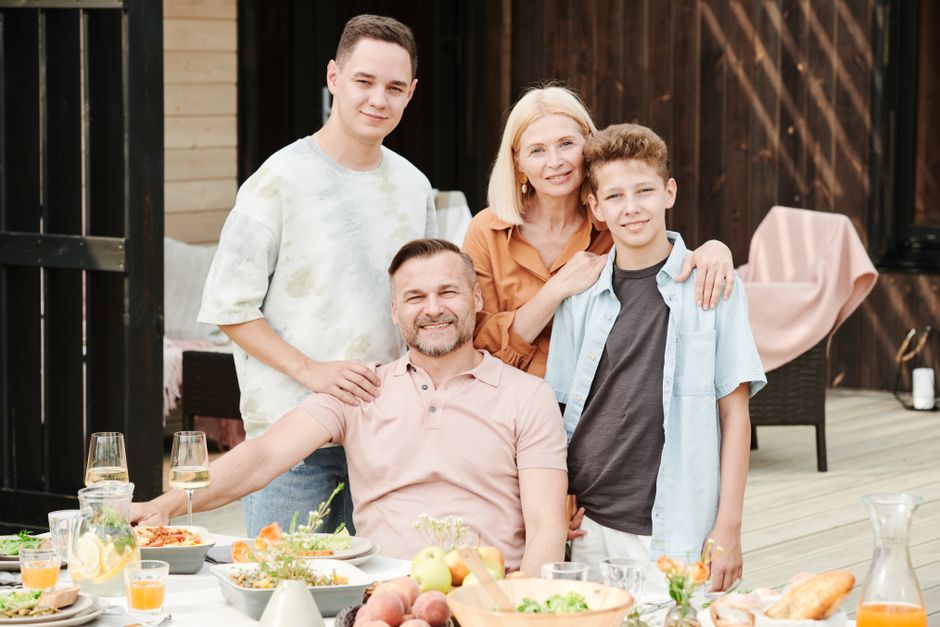 Family of four dining outdoors in a cheerful atmosphere with a table full of food and beverages.