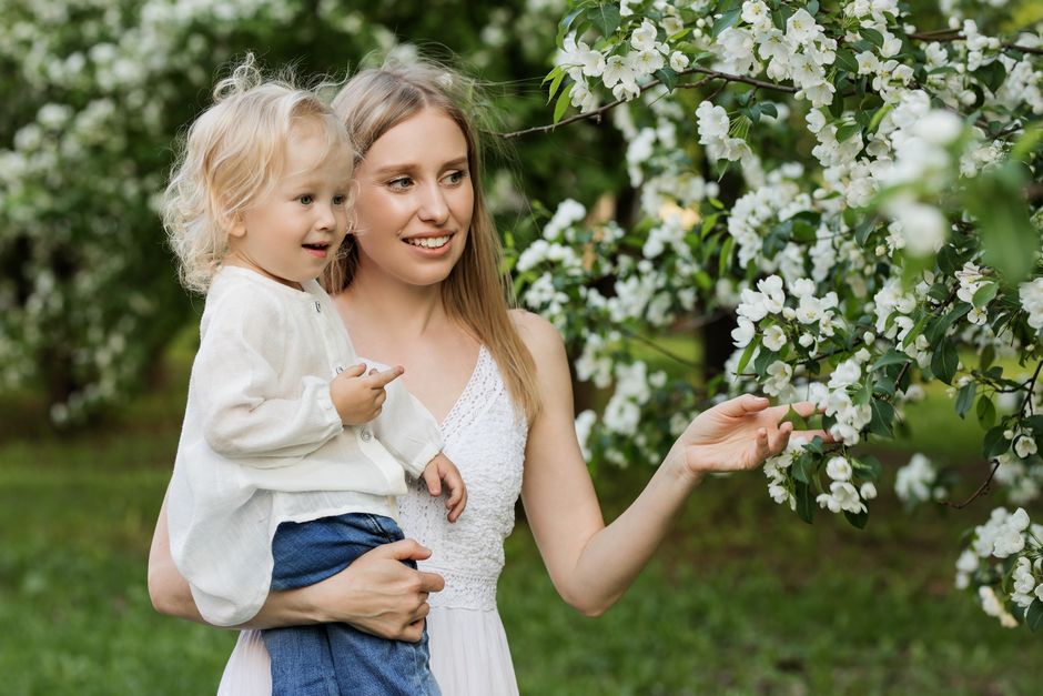 A mother with her young child in a lush orchard full of blooming white flowers, capturing a tender moment.