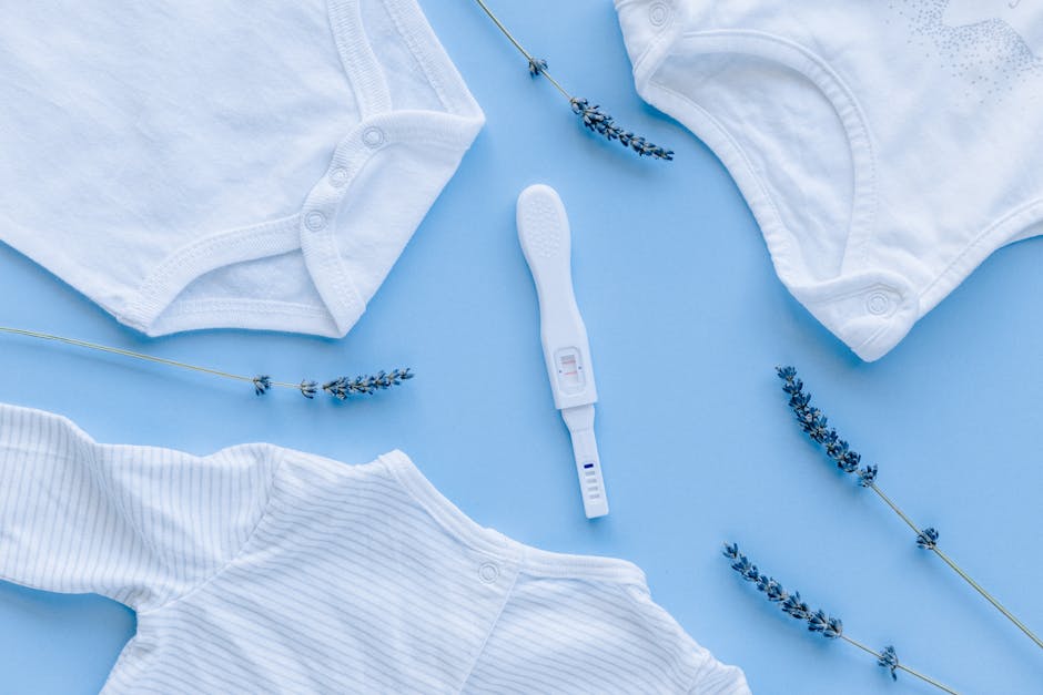 Flat lay of baby clothes and positive pregnancy test on blue background.