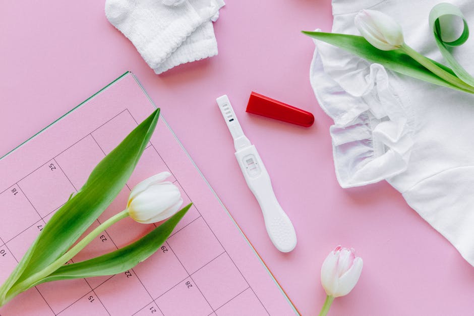 A flat lay scene featuring a pregnancy test with tulips, baby clothes, and a calendar.