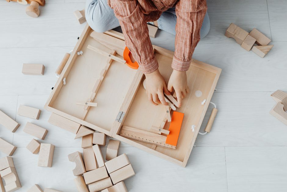 A child playing with wooden blocks and a toy set on a light floor, fostering creativity and fun.