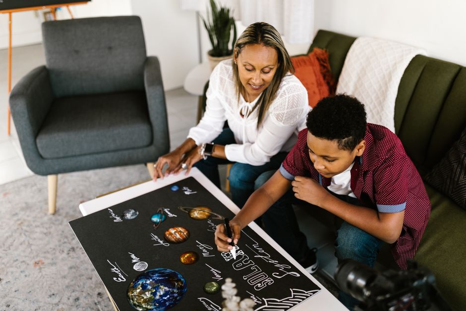 A mother and son collaboratively working on a solar system project indoors.