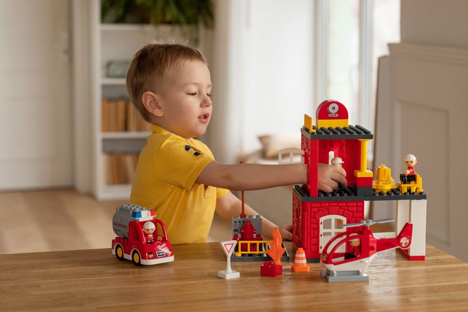 A young boy wearing a yellow shirt engages with a firefighter building block set at home, fostering creativity and fun.
