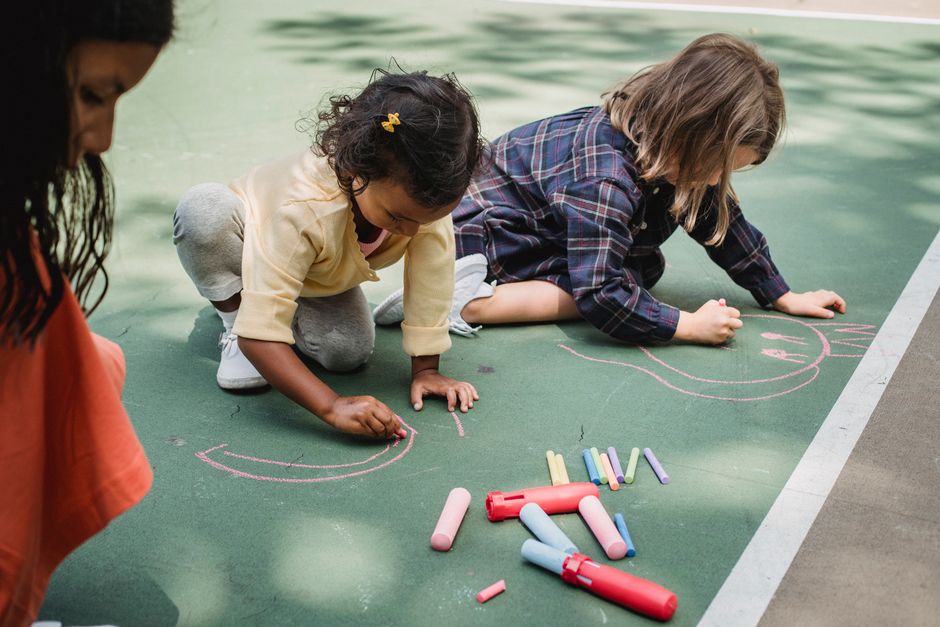 Three children creatively drawing on pavement with colorful chalk outdoors.
