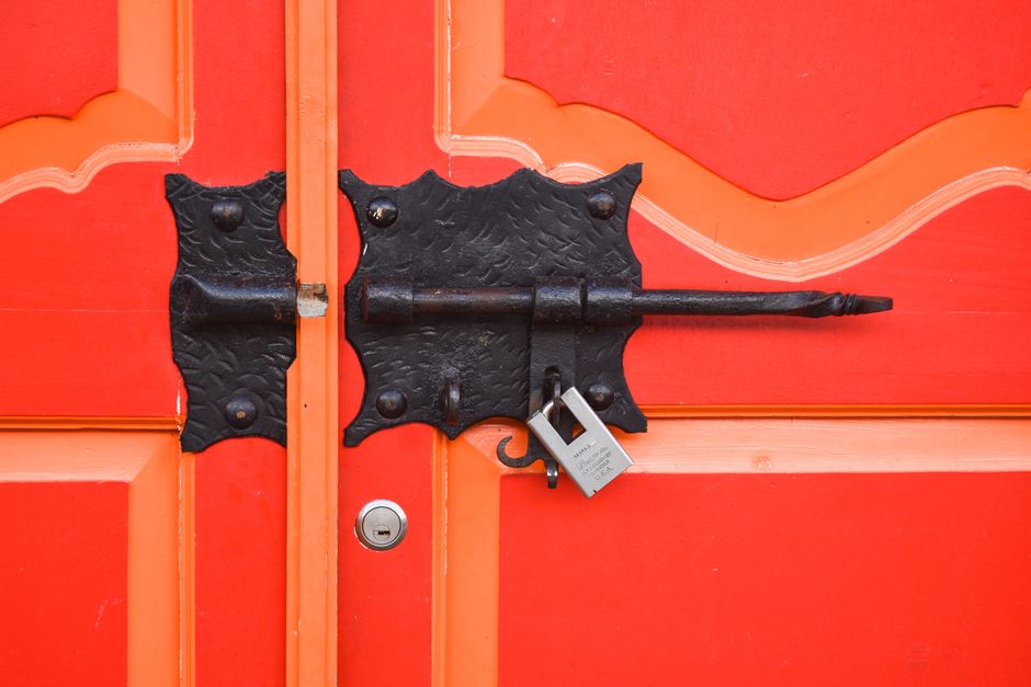 Close-up of a vibrant red door featuring a decorative antique iron lock and padlock.