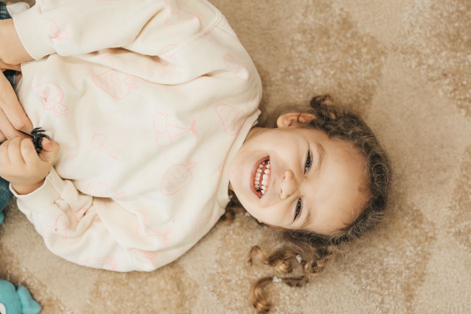 Happy young girl in white sweater smiling while lying on the carpet indoors.