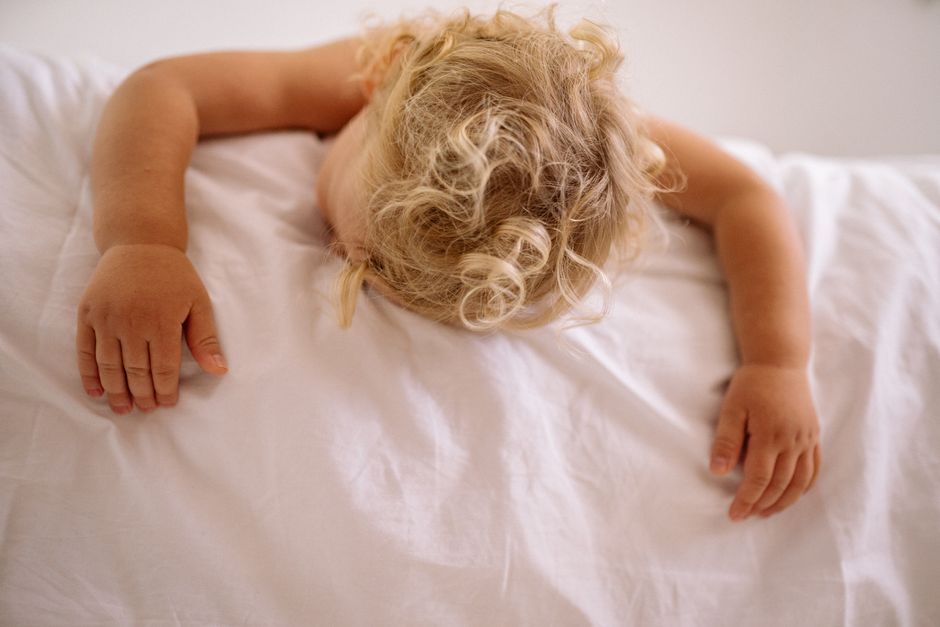 A serene image of a child sleeping face down on a white bed, capturing innocence and tranquility.