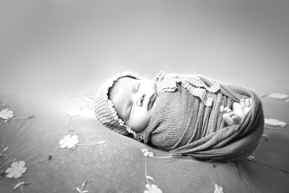 Black and white portrait of a sleeping newborn wrapped in cloth, conveying peace and innocence.