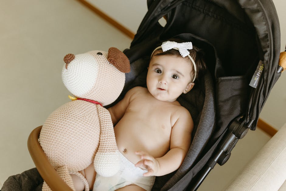 Cute baby with a knitted teddy bear in a stroller, smiling indoors.
